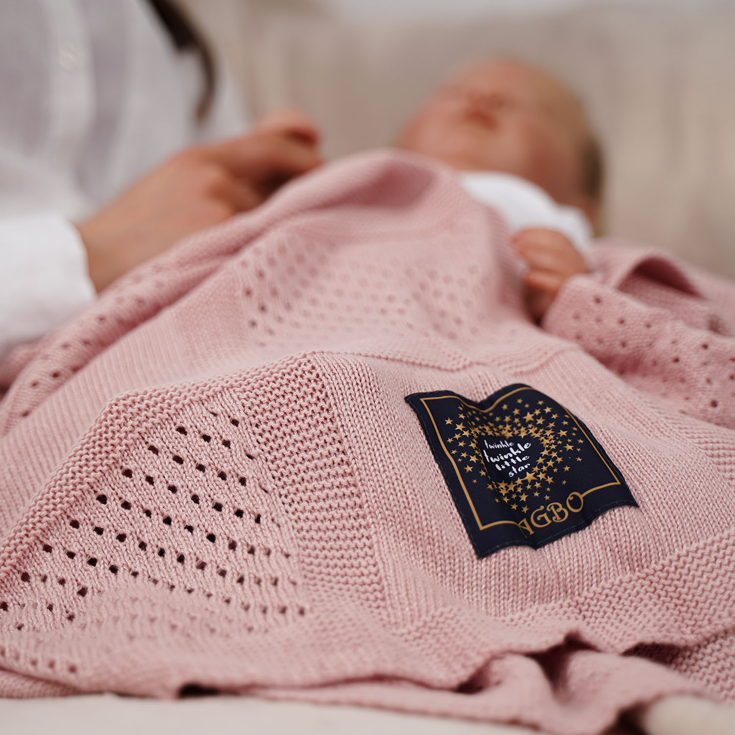 Schlafendes Baby auf den Armen der Mutter unter einer rosa Kinderdecke